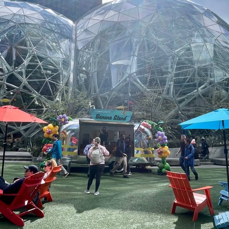 silver food truck with bananas hanging on it parked in front of large glass spheres